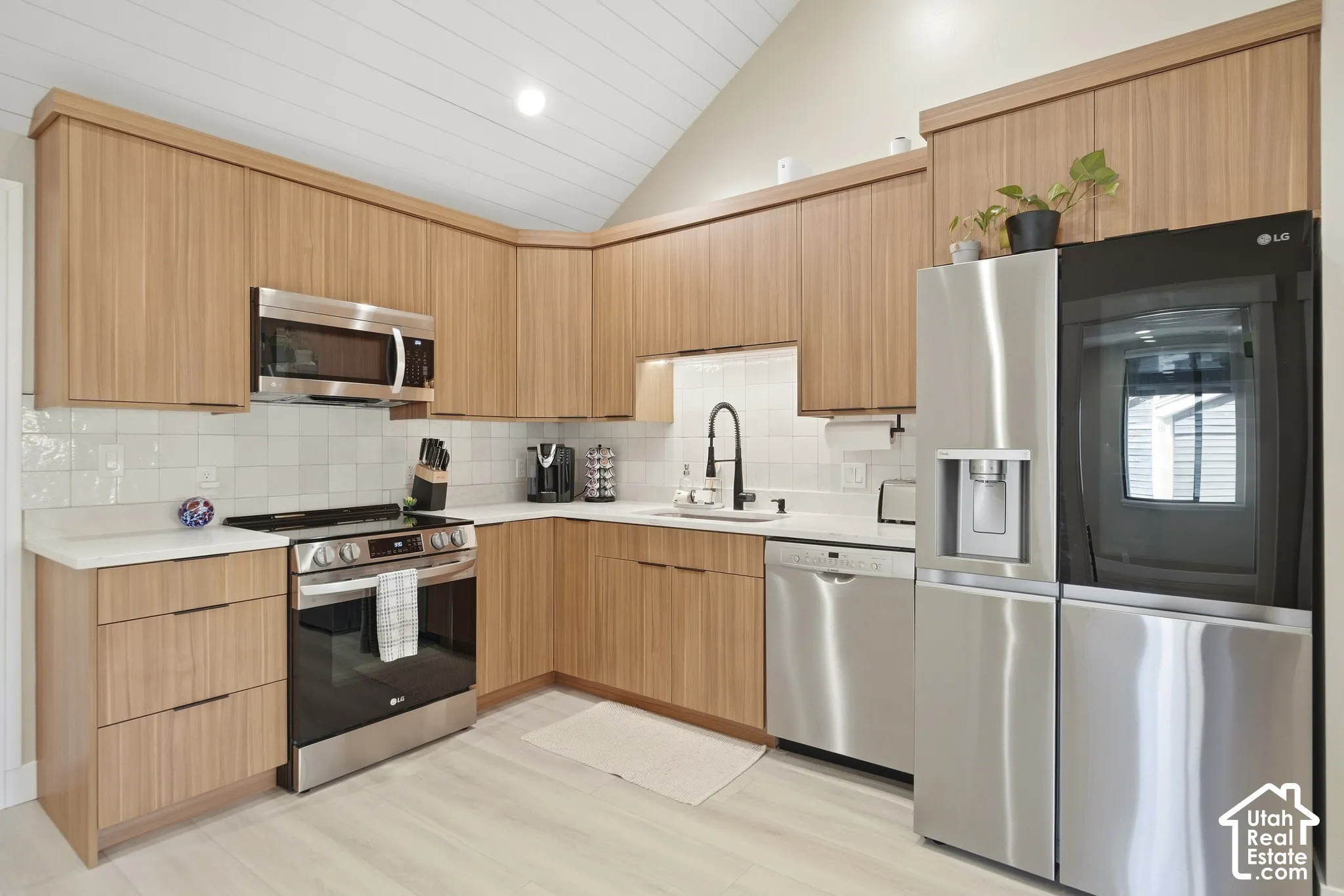 Kitchen featuring wood-finish cabinetry, stainless steel appliances, white tile backsplash, and light-toned flooring