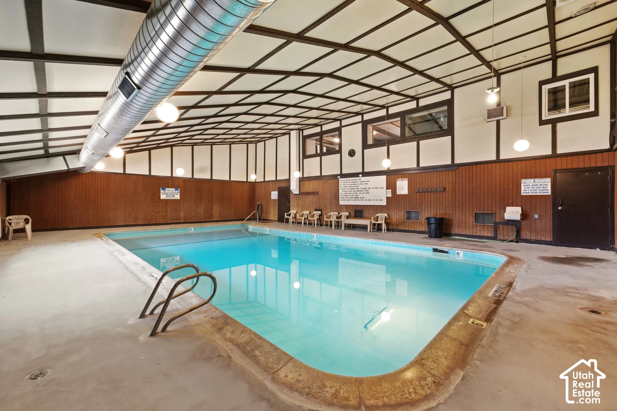 Indoor swimming pool with concrete decking, wood paneling, exposed ductwork, and overhead lighting