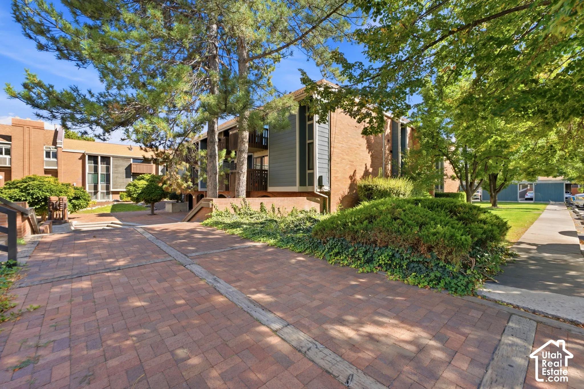 Brick paver pathways surrounded by mature trees, landscaping, and brick exterior buildings