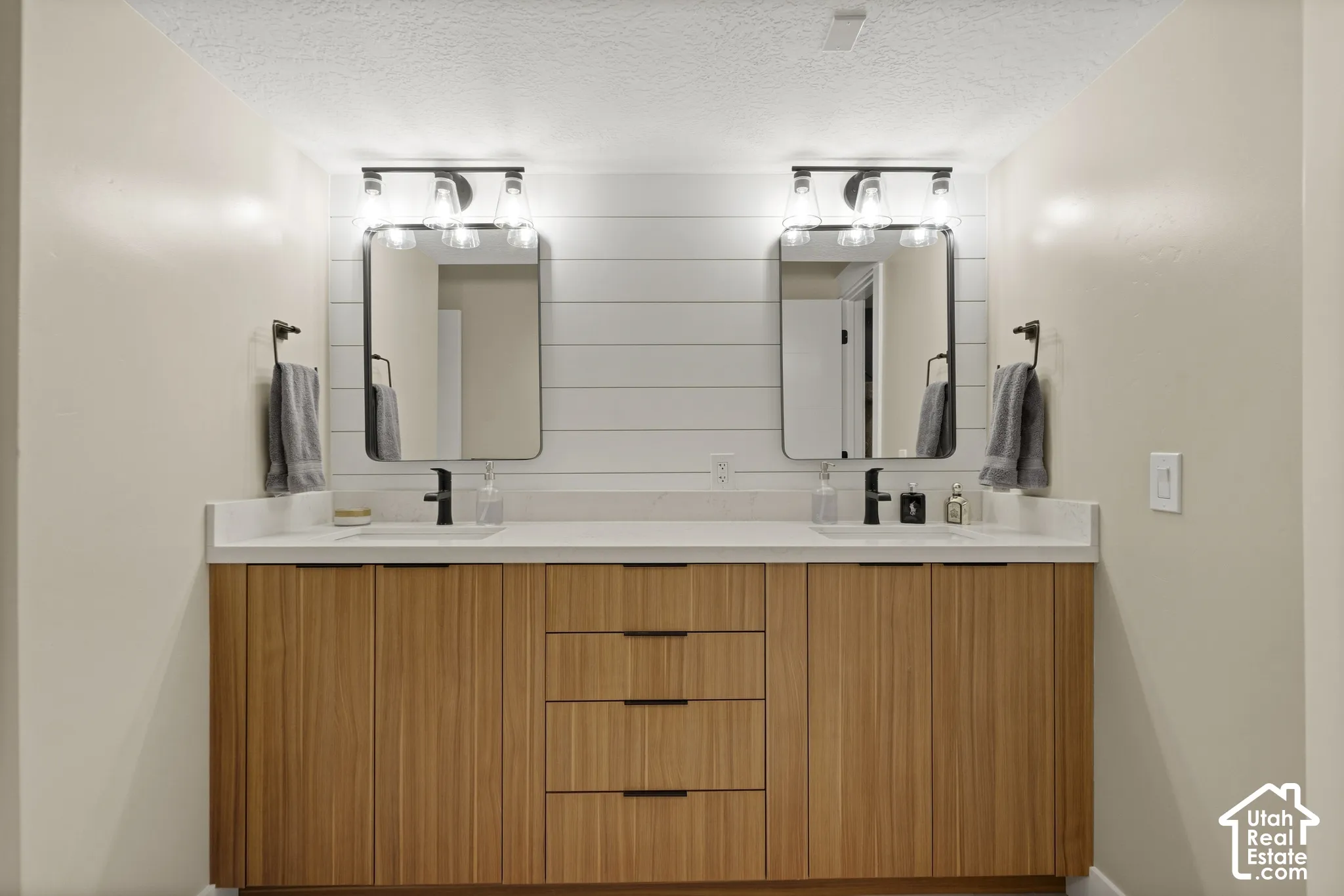 Dual vanity with wood-finish cabinetry, white countertops, and matte black fixtures