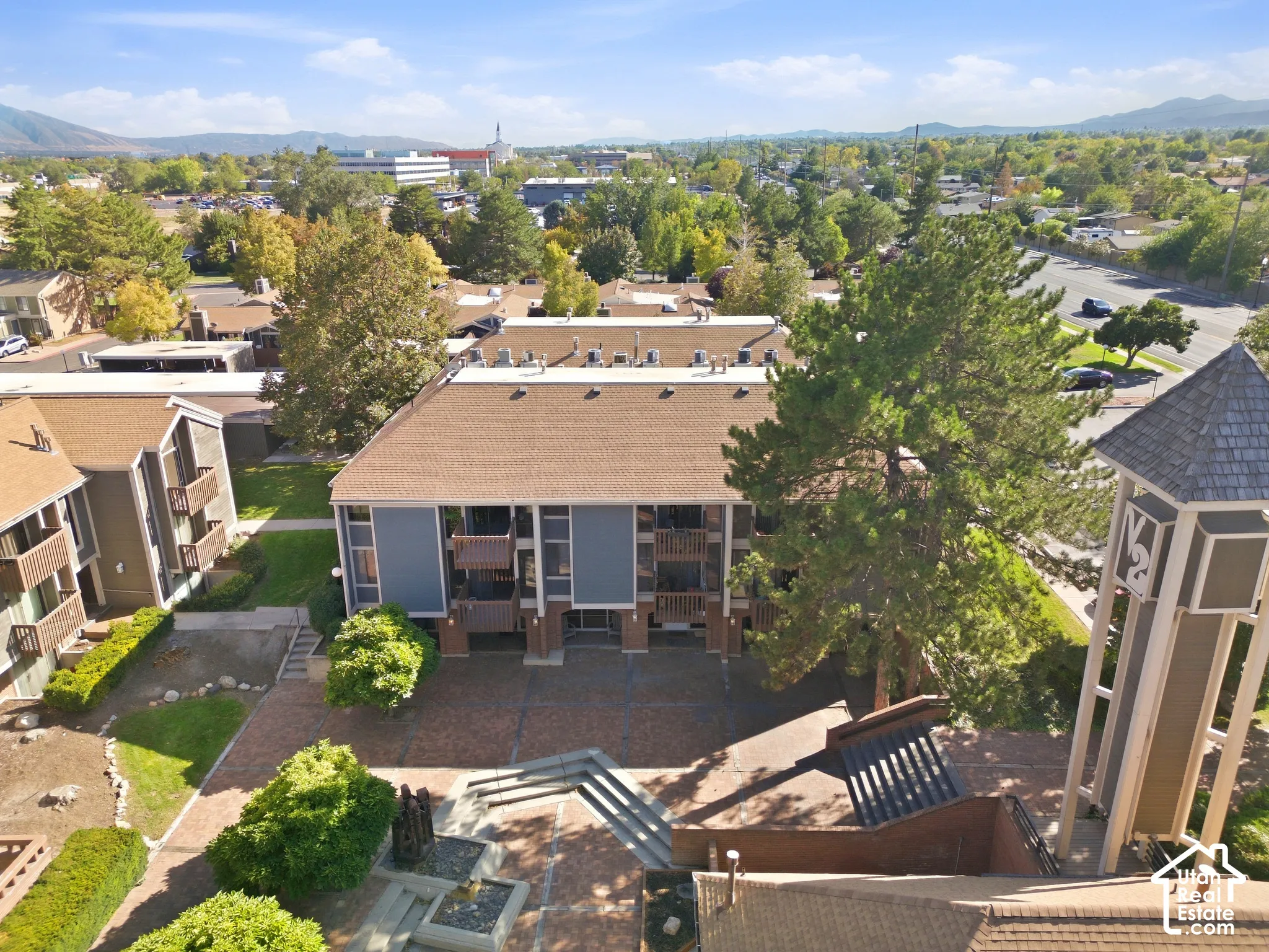 Multi-story building featuring balconies, a paved courtyard with integrated planters, and surrounding green spaces