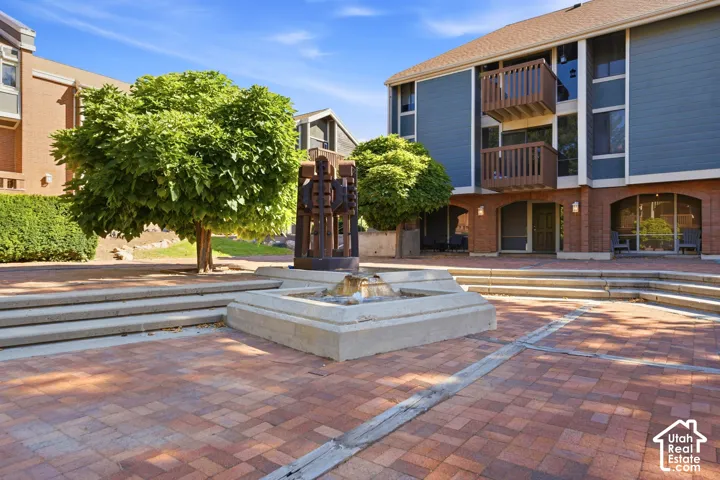Brick paver courtyard with a central fountain, surrounded by mature trees and multi-level buildings featuring balconies