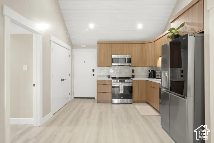 Modern kitchen featuring wood-finish cabinetry, stainless steel appliances, a tile backsplash, and light wood-finish flooring