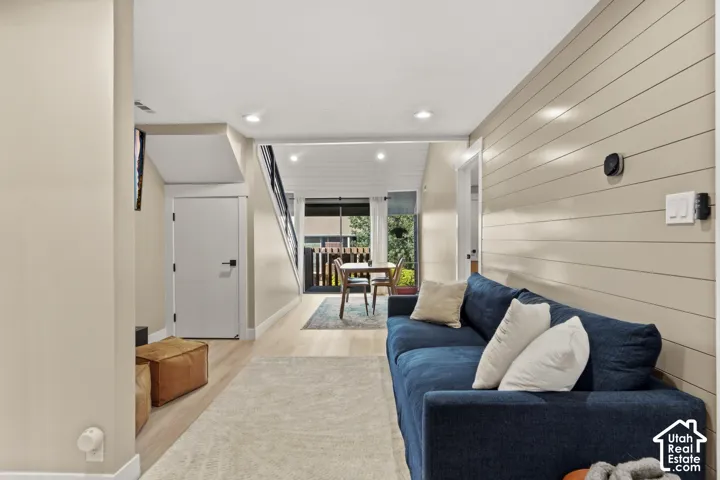 Recessed lighting illuminates the open living area featuring wood-finish flooring, a shiplap accent wall, and a staircase with dark railings