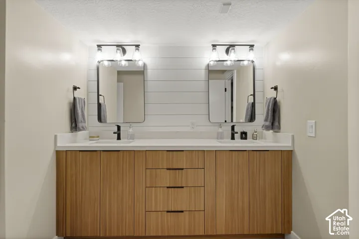 Dual vanity with wood-finish cabinetry, white countertops, and matte black fixtures