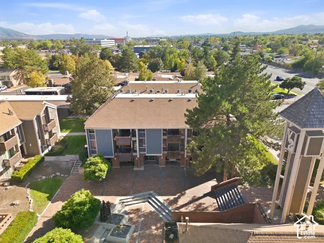 Multi-story building featuring balconies, a paved courtyard with integrated planters, and surrounding green spaces