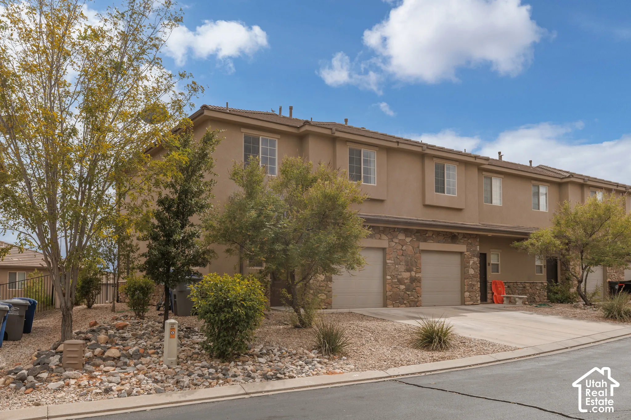 Two-story stucco exterior with stone accents, attached garages, and a paved driveway