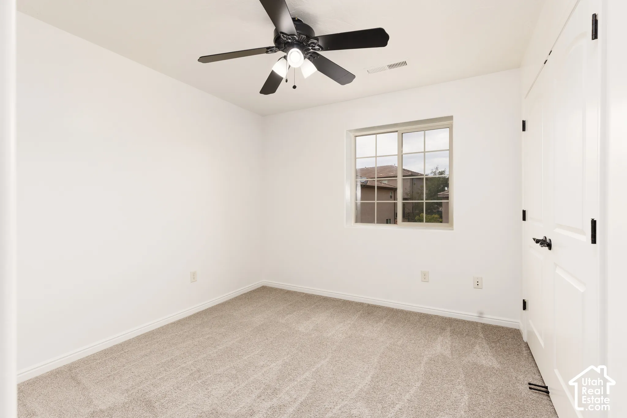 Neutral wall tones, gray carpet, black ceiling fan, white paneled doors, and a multi-pane window