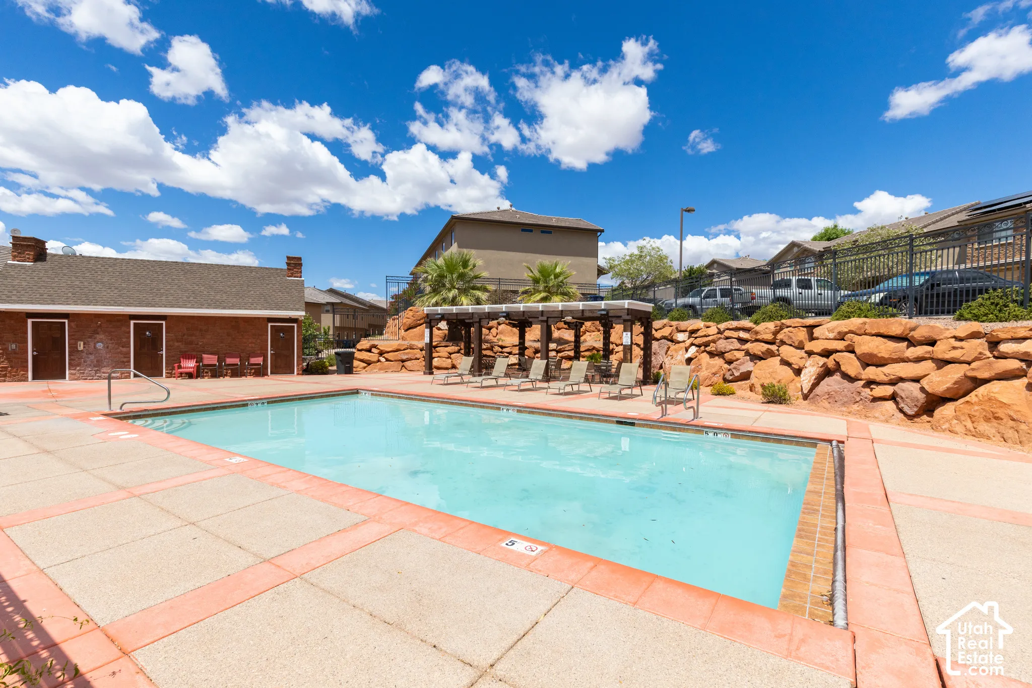 Outdoor swimming pool with concrete decking, a pergola, and a rock retaining wall