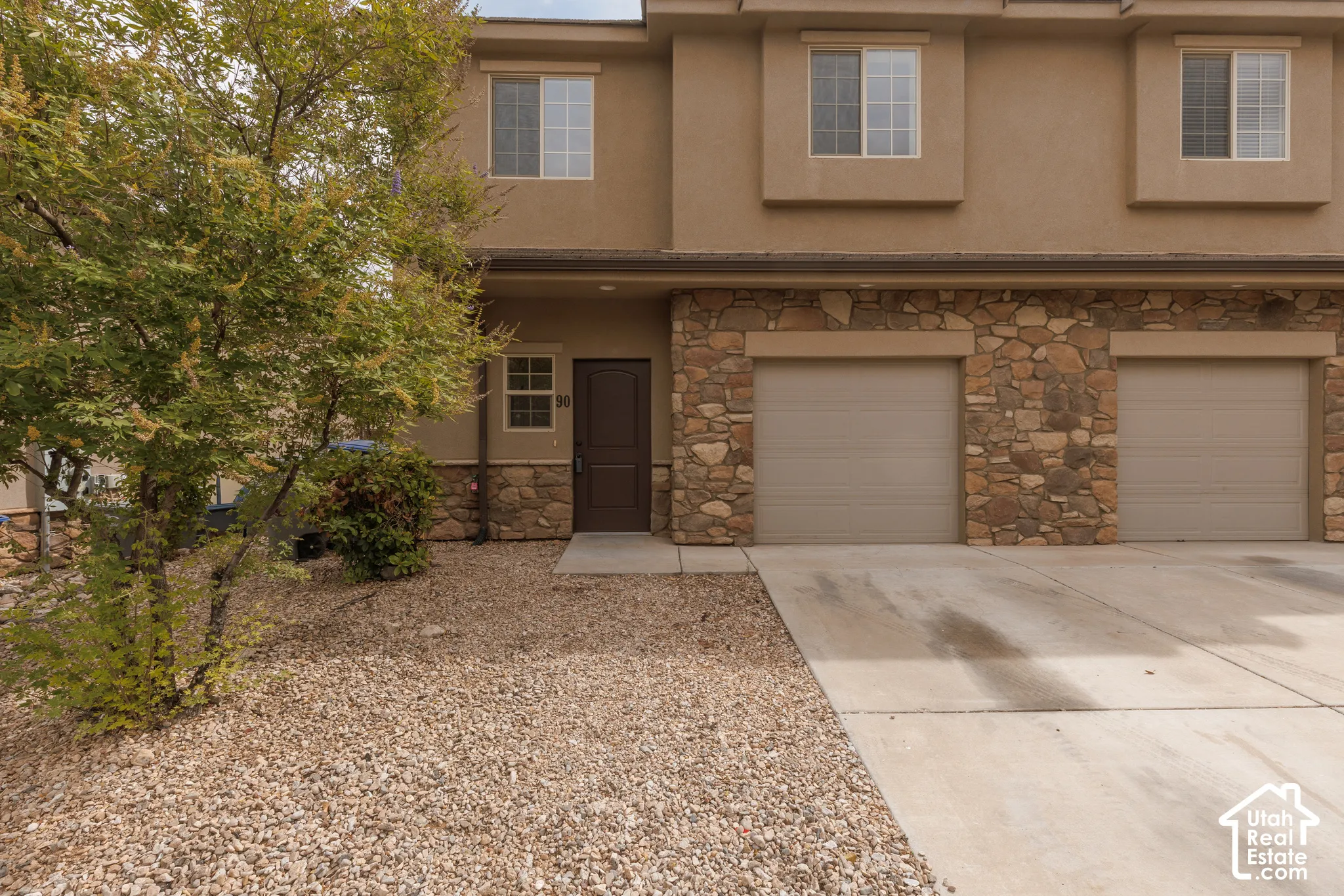 Stucco exterior with stone accent facade, two-car attached garage, concrete driveway, and front entry door