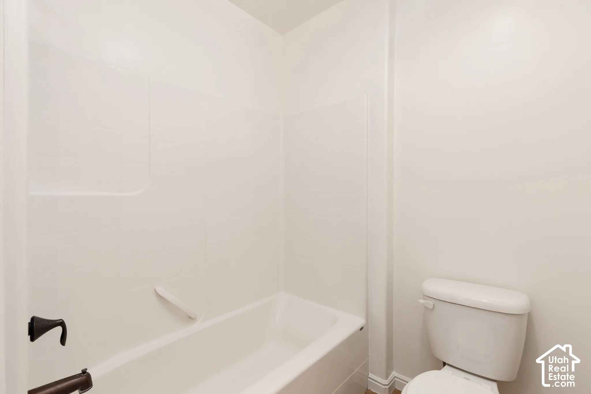 White bathtub with integrated shower surround, dark bronze fixtures, and white toilet