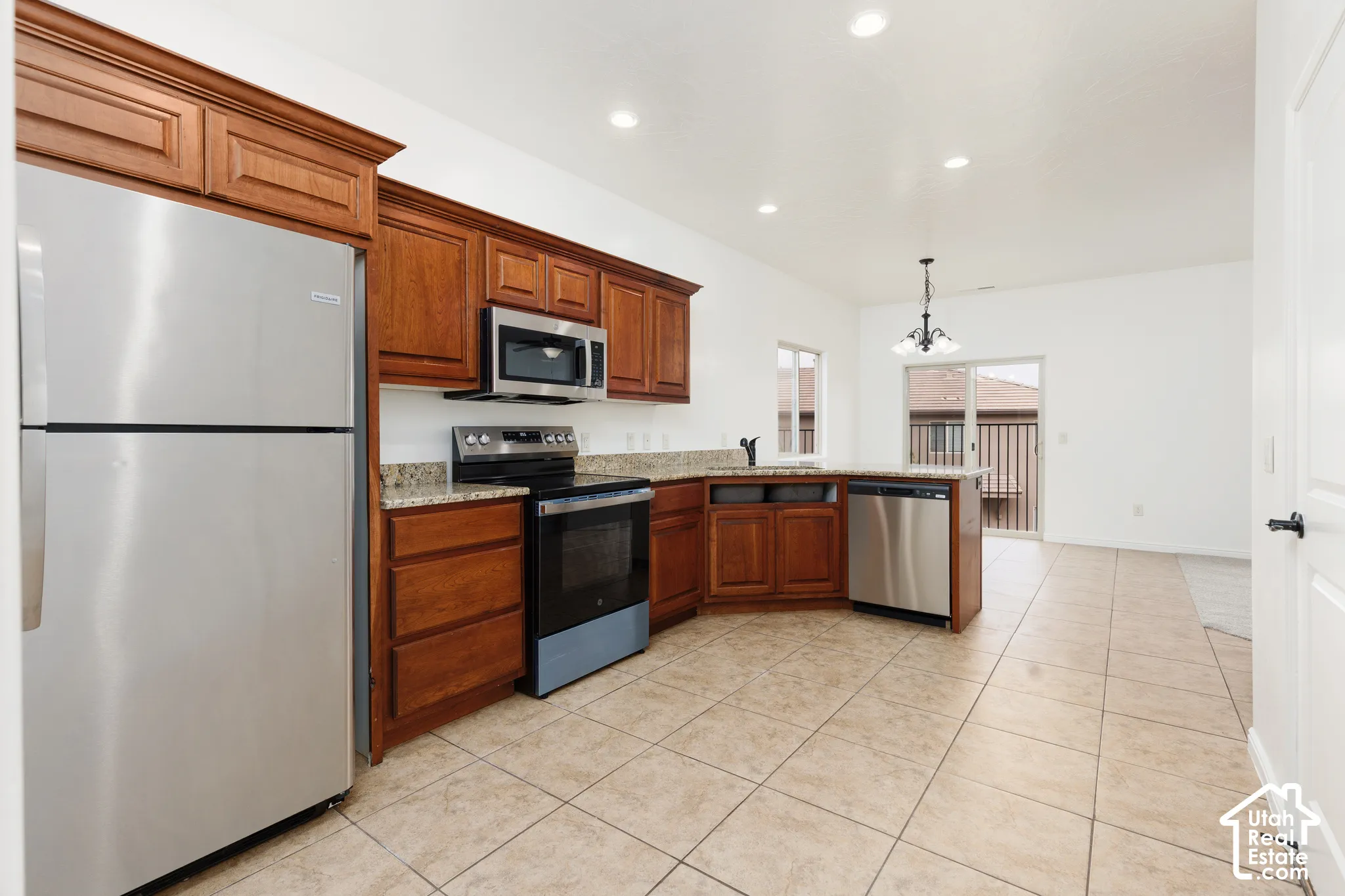 Kitchen with wood cabinetry, stainless steel appliances, granite countertops, and tile flooring