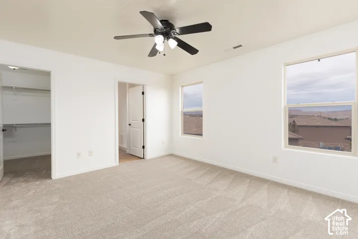 Neutral tone carpet flooring, white walls, two windows, ceiling fan with light fixture, and an open closet with shelving and hanging rods