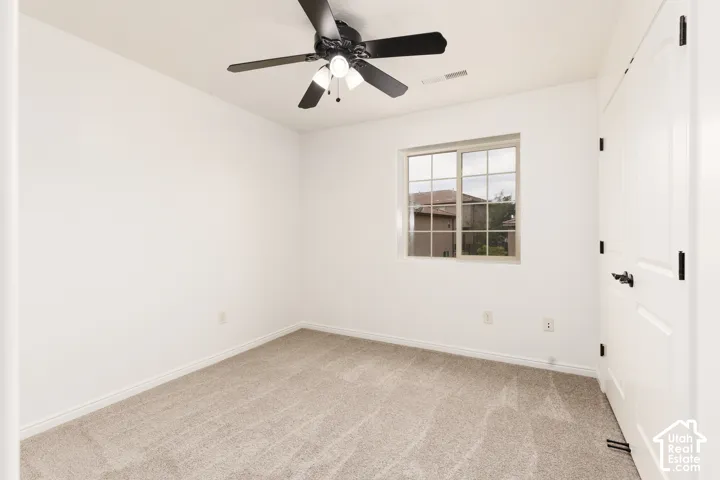 Neutral wall tones, gray carpet, black ceiling fan, white paneled doors, and a multi-pane window