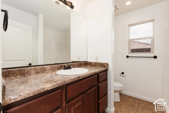 Vanity with a composite countertop and integrated sink, dark wood-finish cabinetry, rectangular mirror, and overhead vanity lighting