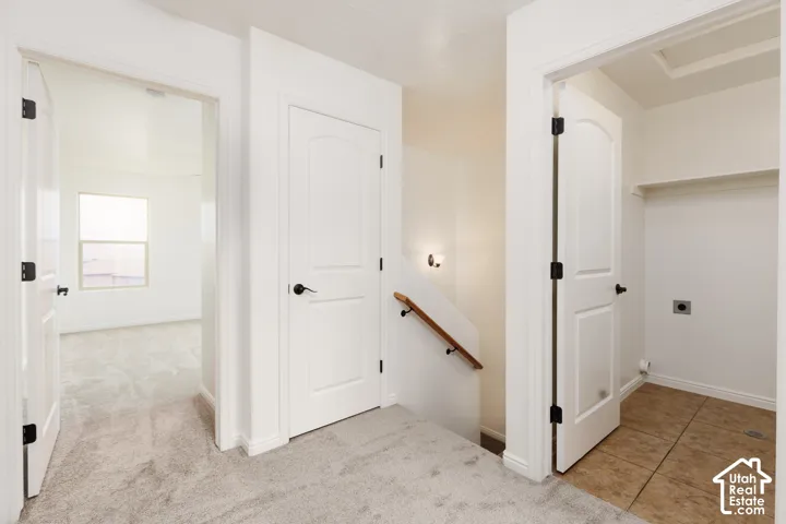 Plush carpeting, white paneled doors with black hardware, hallway sconce lighting, and a tiled utility area with shelving