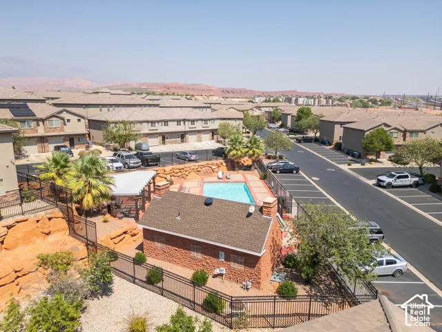 Community pool with a surrounding paved deck, adjacent shaded seating area, and a brick-clad pool house
