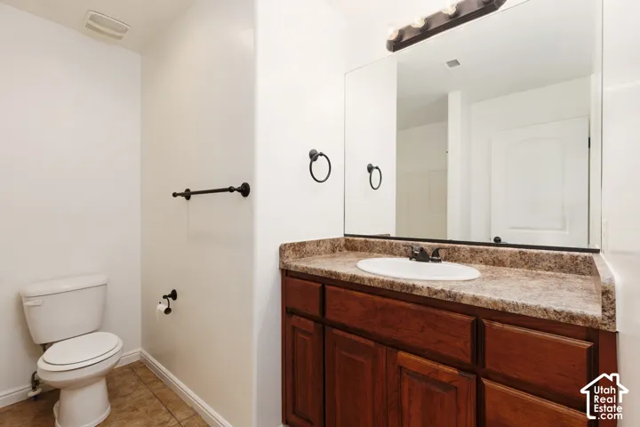 Bathroom featuring a wood-finish vanity with a single basin sink, laminate countertop, and tile flooring
