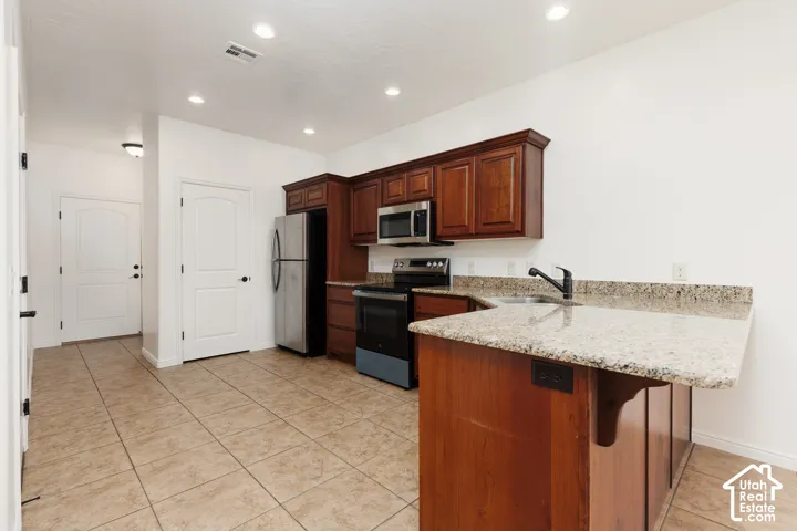 Kitchen featuring wood-finish cabinetry, light-toned stone-look countertops, stainless steel appliances, and tile flooring