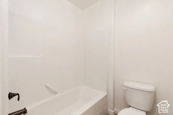 White bathtub with integrated shower surround, dark bronze fixtures, and white toilet