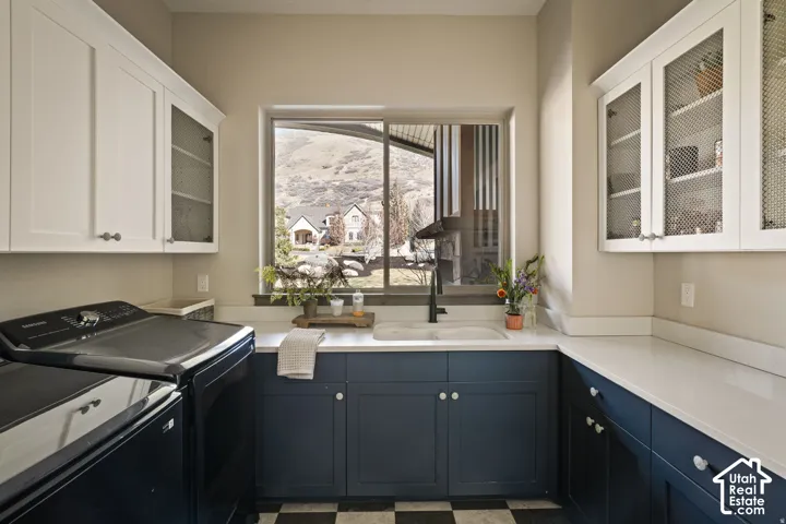 White upper cabinetry with glass-front doors, dark blue lower cabinetry, white solid surface countertops, single-basin sink with a black gooseneck faucet, and checkered tile flooring