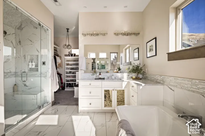 Tiled walk-in shower with glass enclosure and built-in bench, freestanding soaking tub with deck-mounted faucet, dual vanity with undermount sinks and extensive countertop space, tiled flooring, and a dedicated closet area