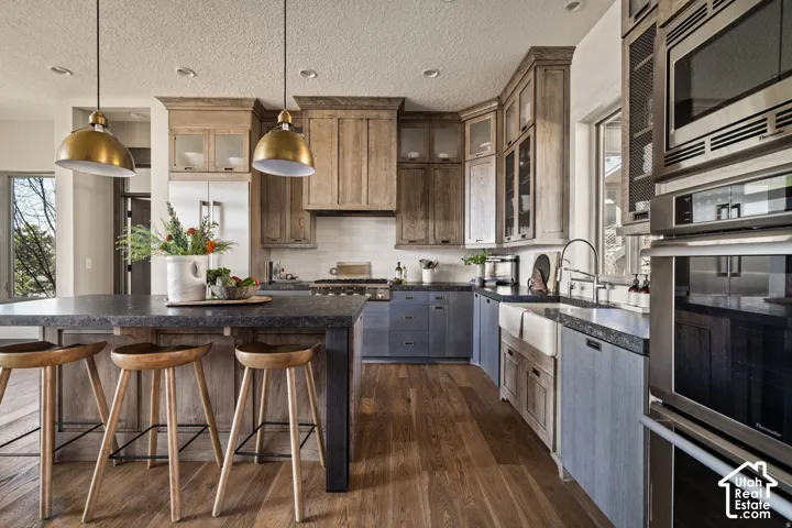 Open-concept kitchen featuring wood-finish flooring, a large island with dark countertops, mixed-tone cabinetry, and integrated stainless steel appliances