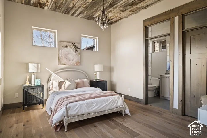 Wood-finish flooring, accent ceiling with wood-finish planks, recessed windows, built-in bathroom vanity, and chandelier