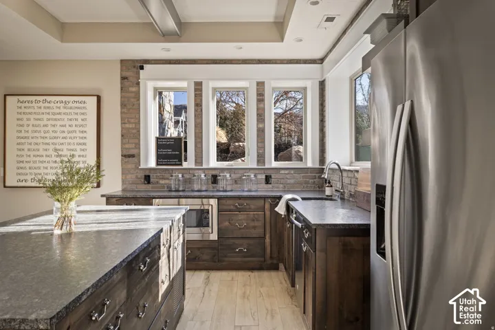 Exposed brick backsplash, dark wood-finish cabinetry, stainless steel appliances, and a recessed ceiling with integrated lighting