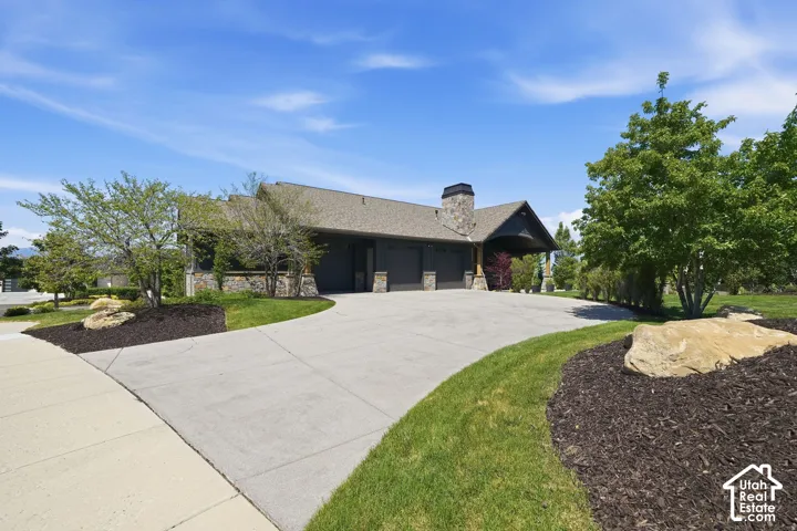Expansive concrete driveway, stone facade elements, mature trees, and landscaping with decorative rock features