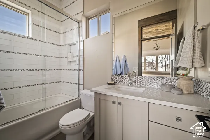 Bathroom featuring a tiled tub-shower combination with a glass enclosure, single vanity with a mosaic tile backsplash, and a contemporary mirror with a dark wood frame