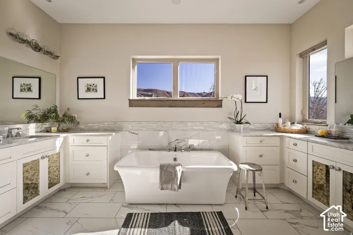 Freestanding bathtub with marble-look surround, dual vanities with integrated sinks, and white cabinetry