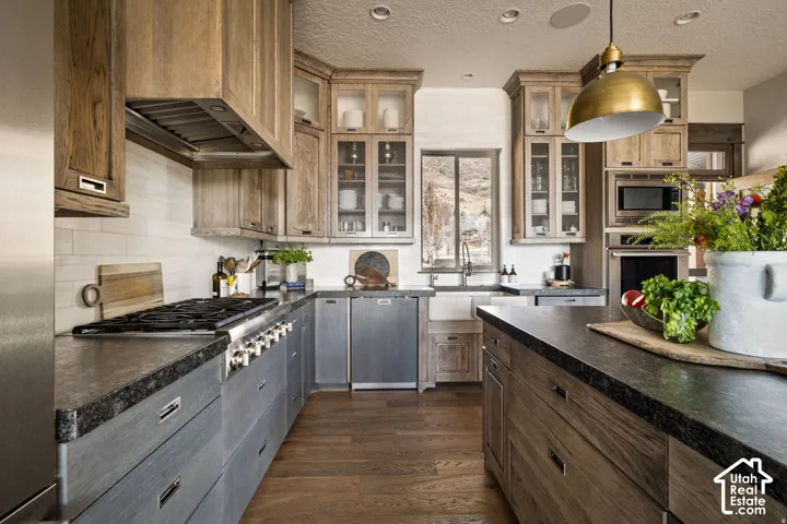 Wood-finish flooring, dark stone countertops, stainless steel appliances, white subway tile backsplash, and a farmhouse sink