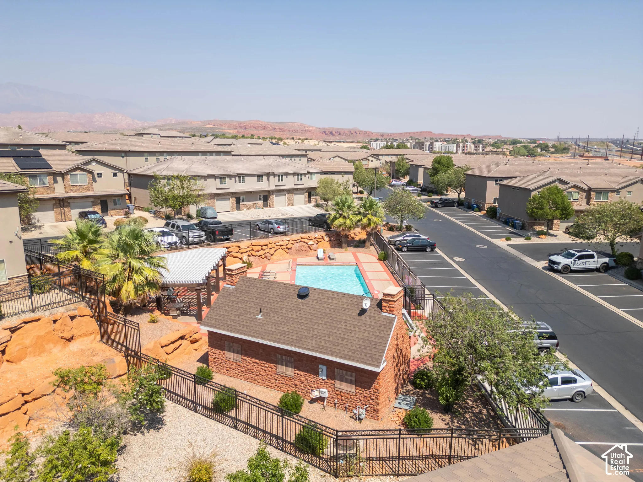 Community pool with a surrounding paved deck, adjacent shaded seating area, and a brick-clad pool house