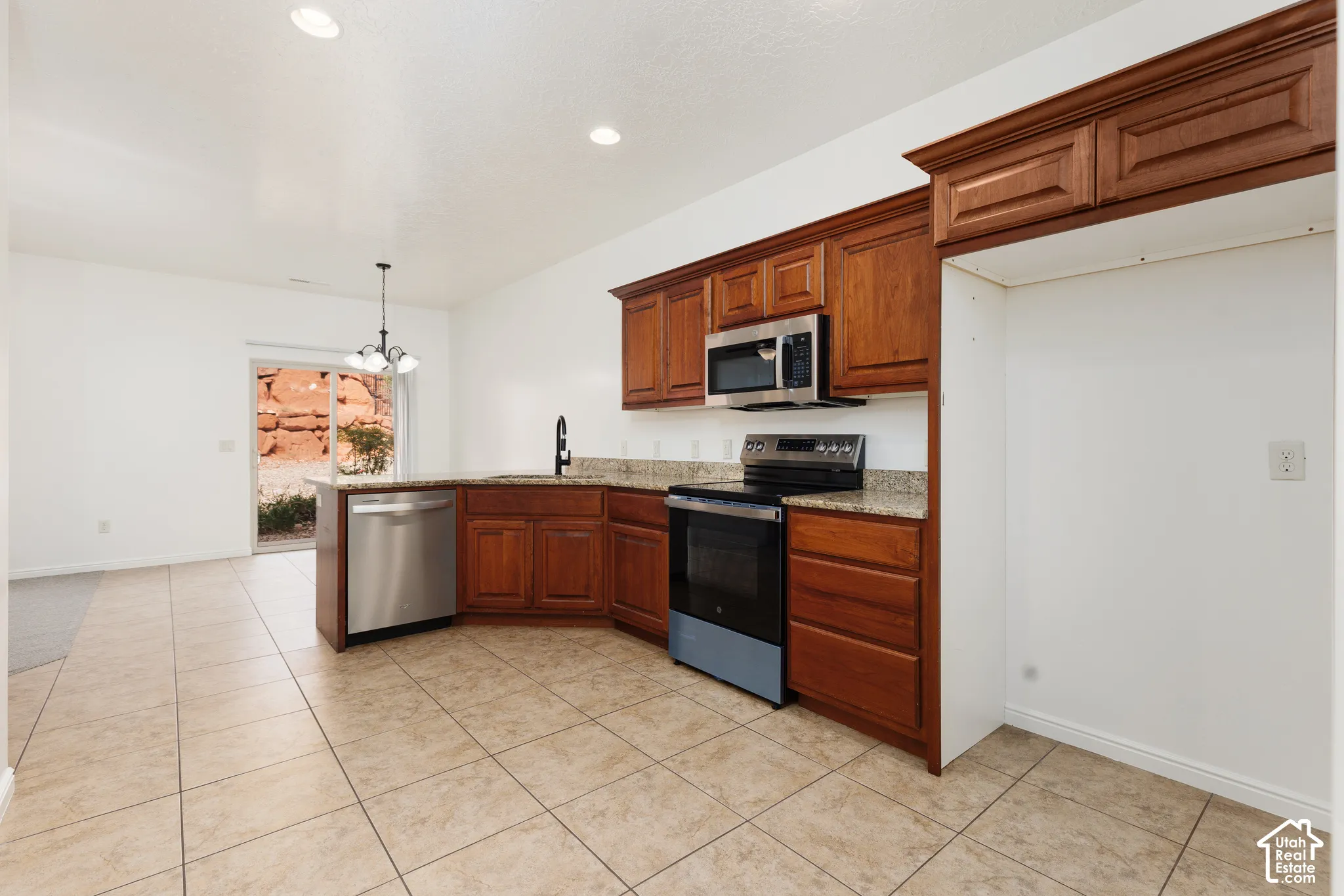 Kitchen featuring wood cabinetry, stainless steel appliances, speckled countertops, and tile flooring