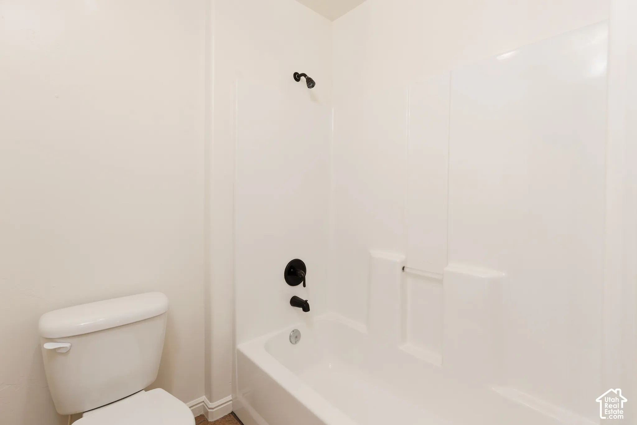 White bathtub with integrated shower, dark bronze fixtures, and a white toilet