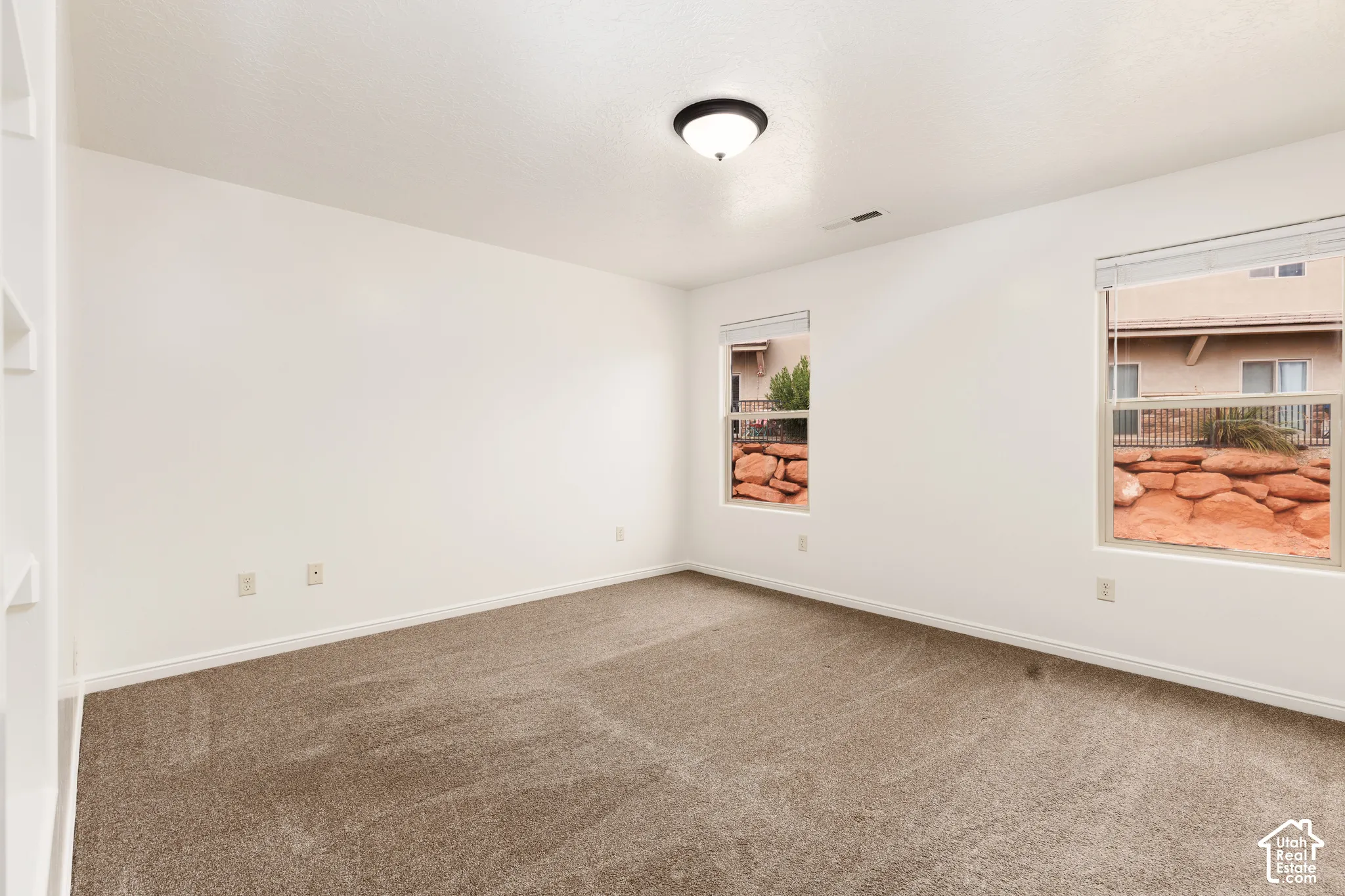Recessed built-in shelving, neutral-toned carpeting, white walls, and two windows with blinds