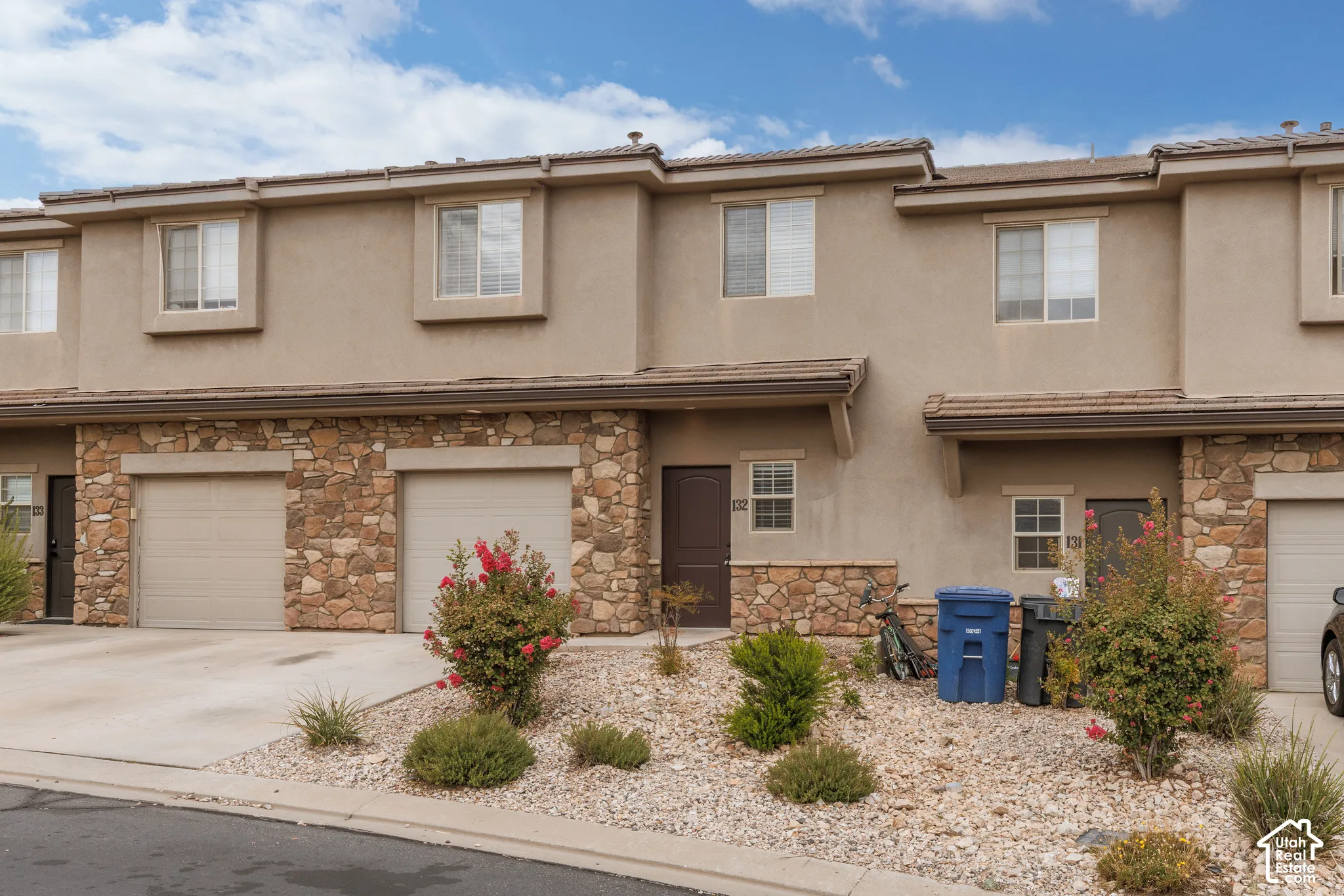 Stucco exterior with stone veneer accents, two integrated garages, and a paved driveway