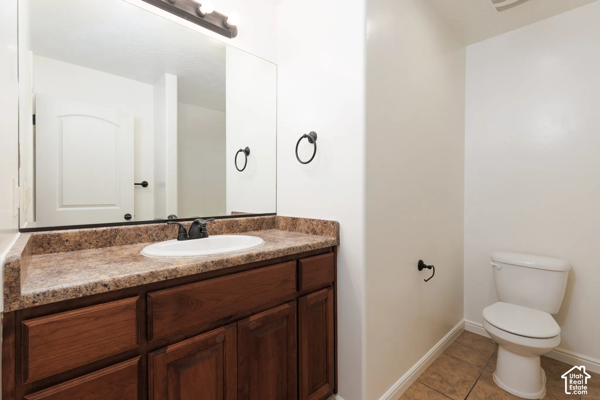 Bathroom featuring a wood-finish vanity with a built-in sink, stone-look countertop, and tile flooring