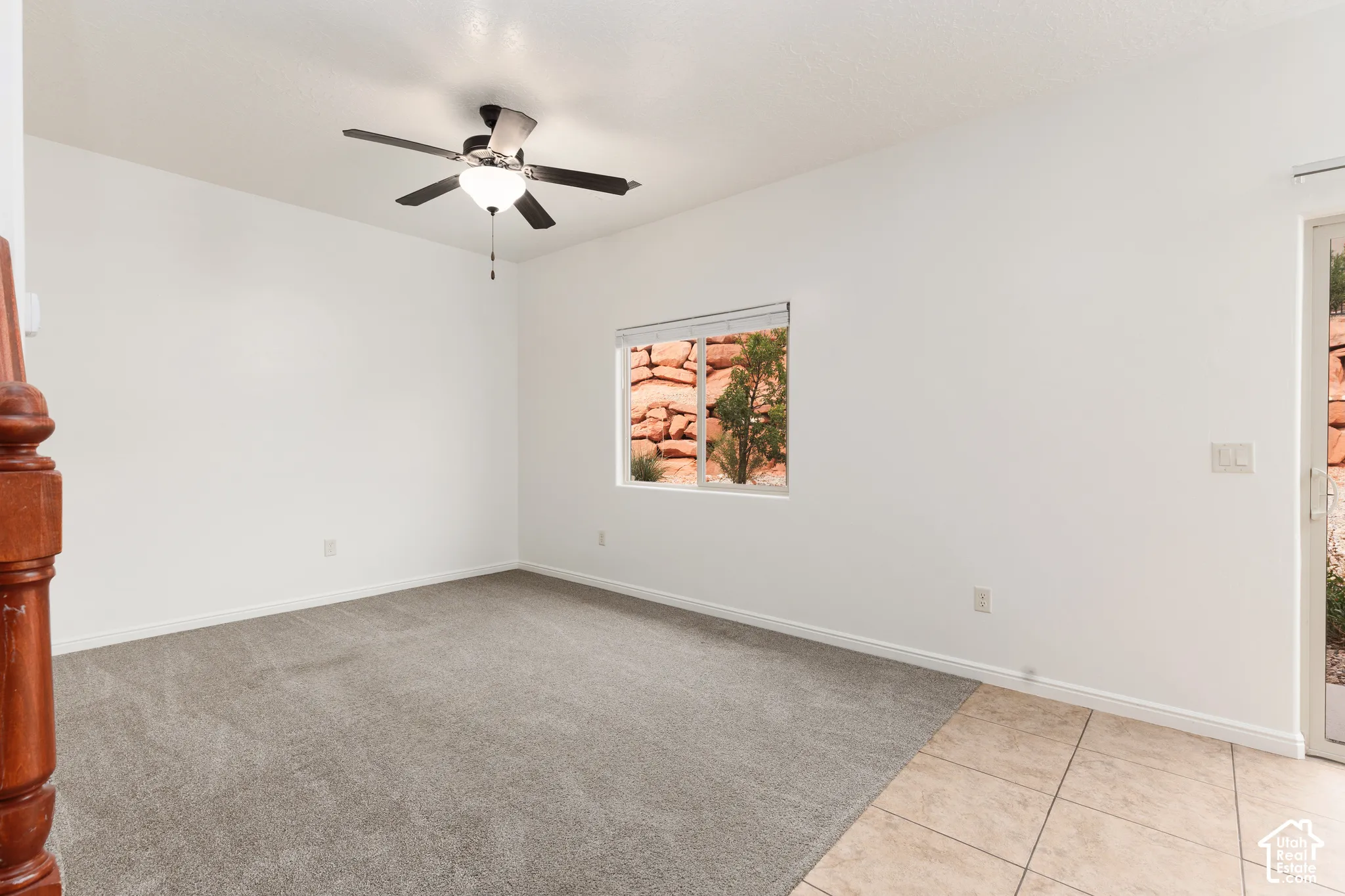 Expansive room featuring a ceiling fan with integrated lighting, a window with exterior rock formations, a glass-paned door, carpeting, and tile flooring