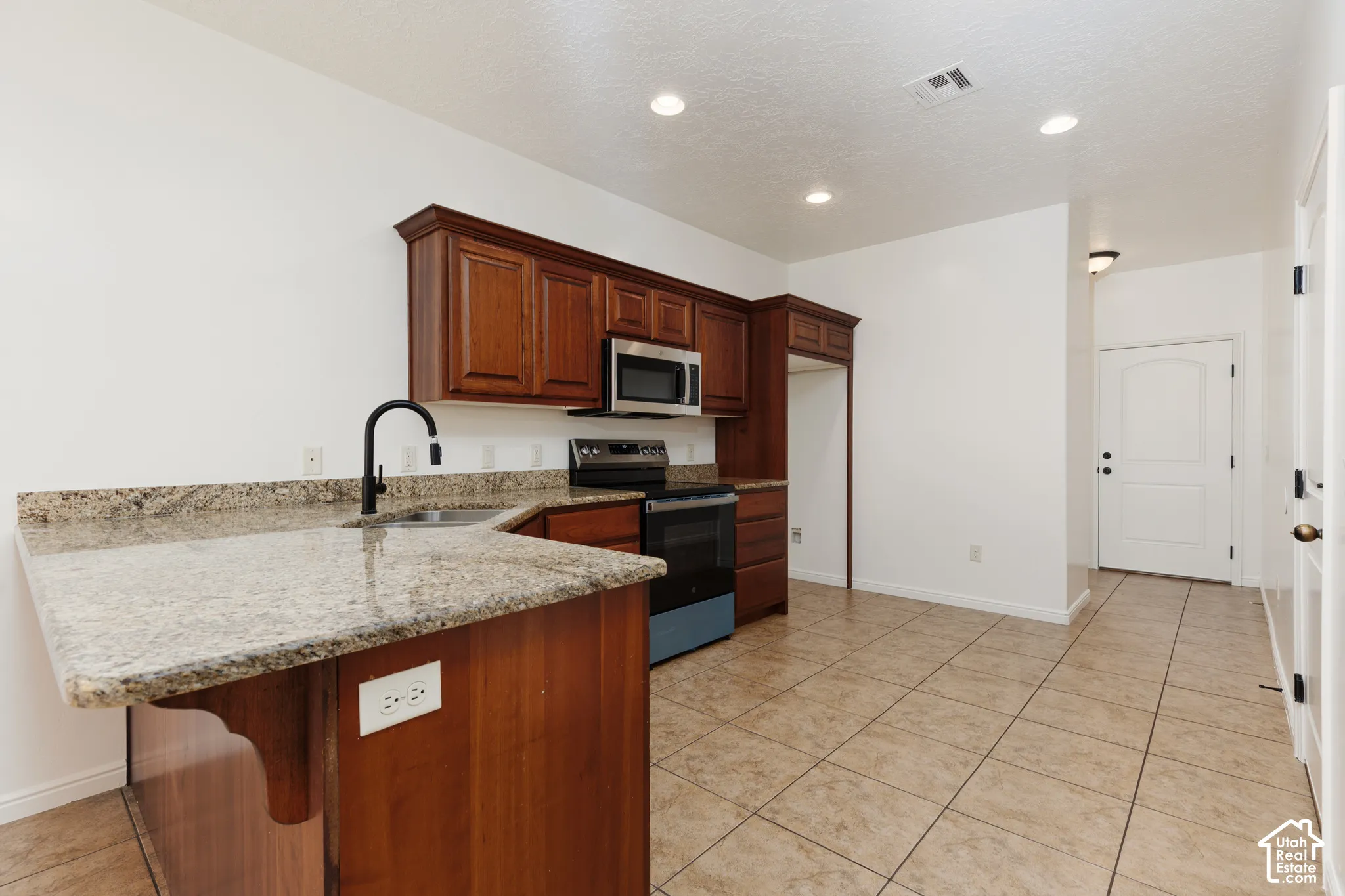 Kitchen featuring wood cabinetry, light-toned countertops, a stainless steel microwave, black range, and tile flooring