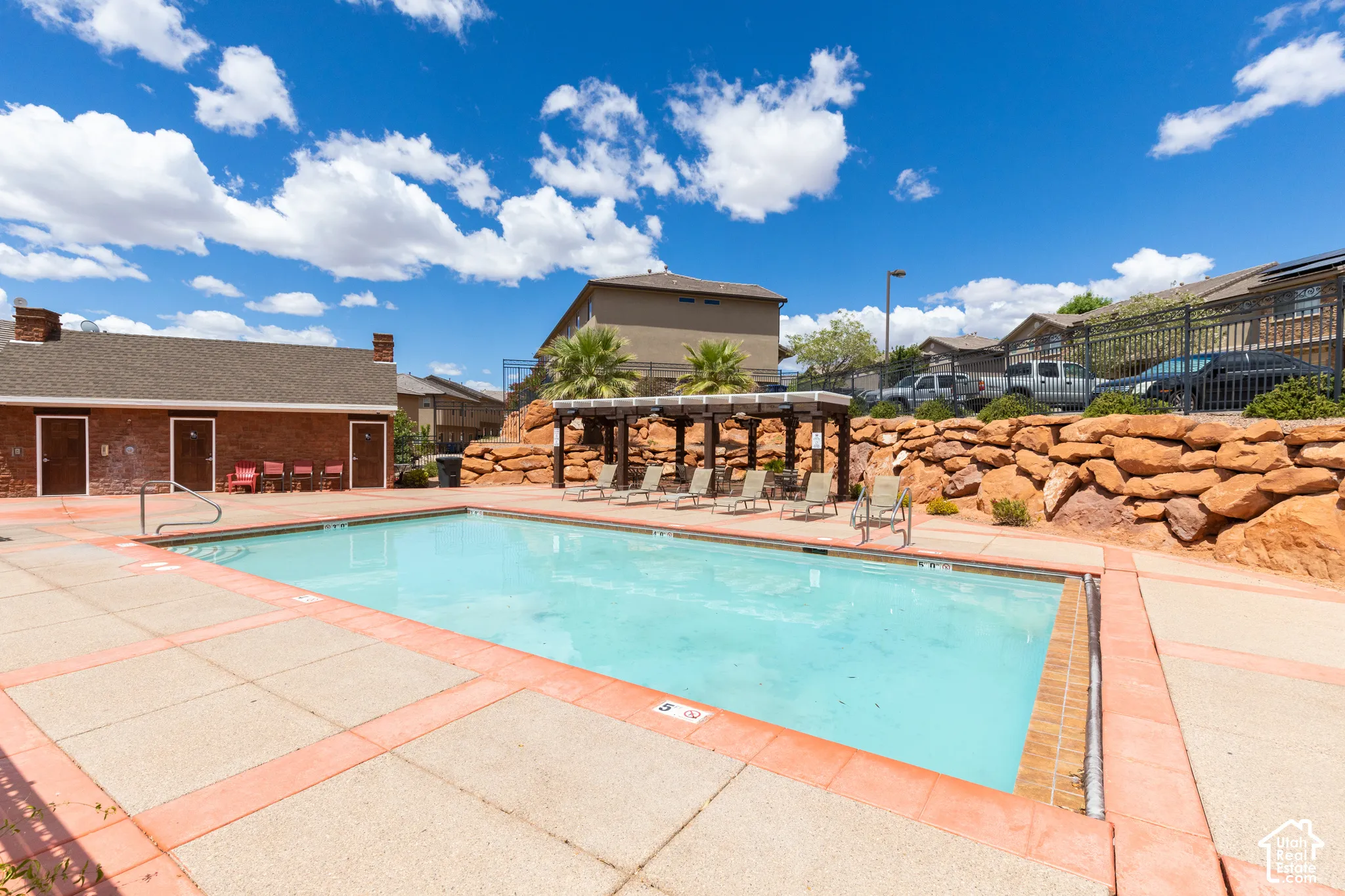 Outdoor swimming pool with concrete decking, a pergola, and a rock retaining wall