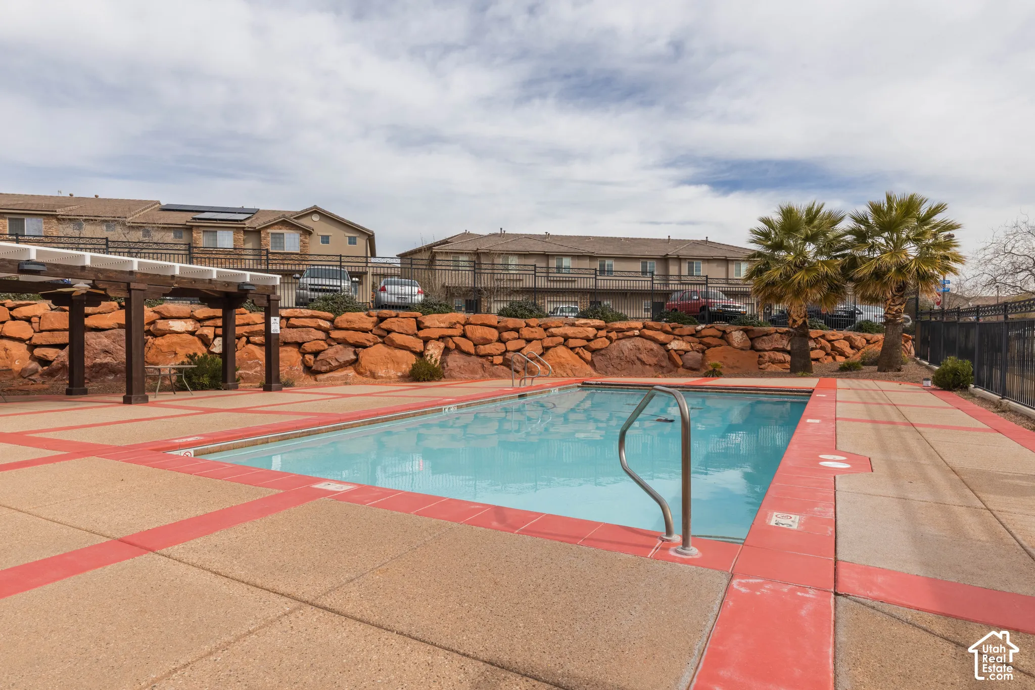 Outdoor pool featuring an integrated metal handrail, surrounded by a concrete deck with red accent borders