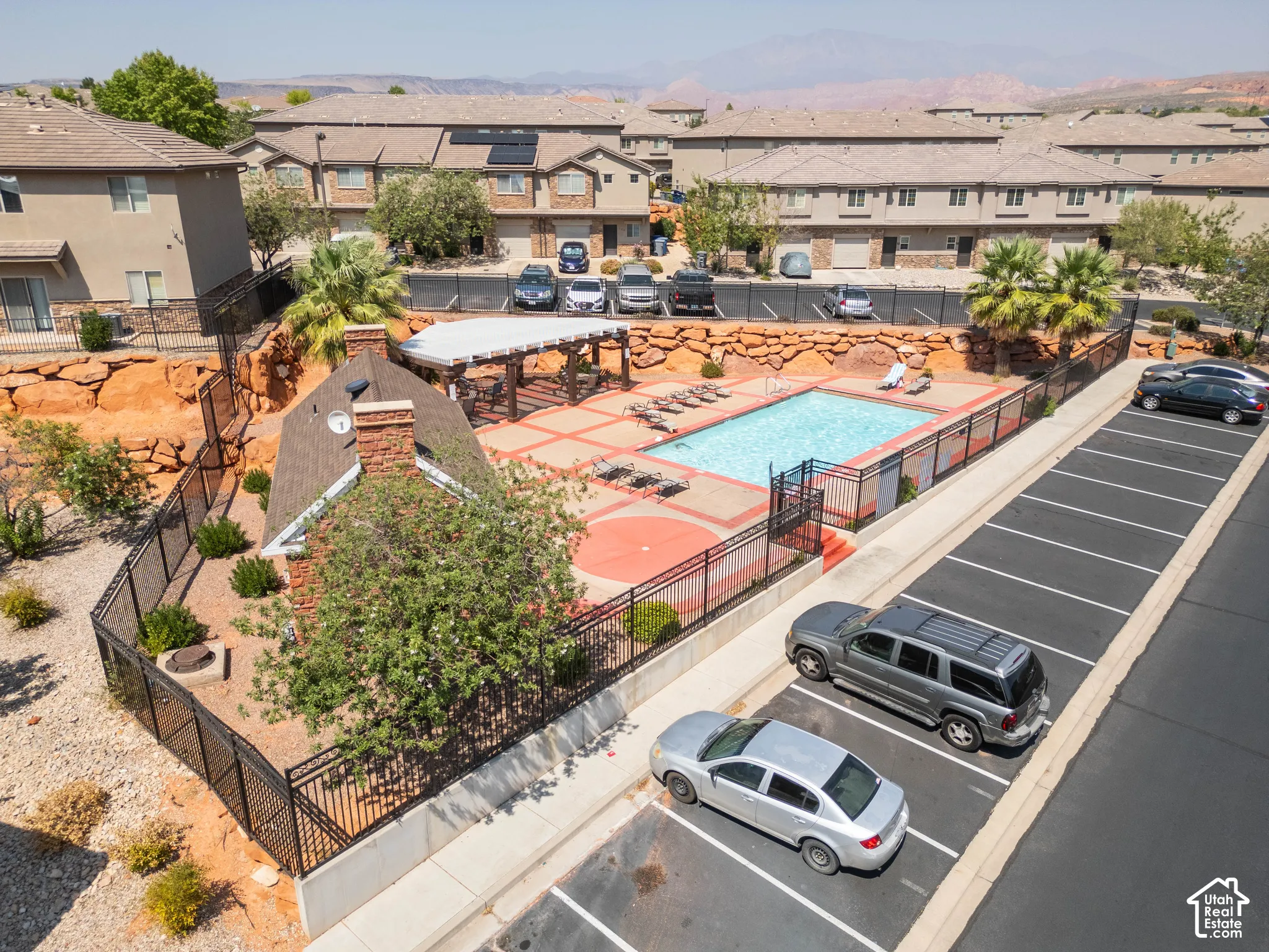 Community pool with surrounding patio, covered lounge area, brick chimney structure, and perimeter fencing
