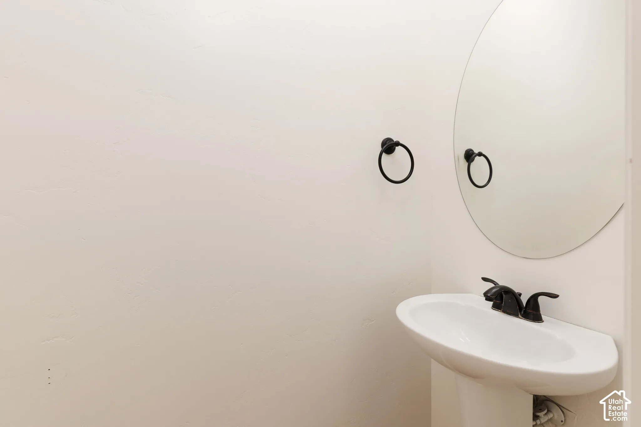 Pedestal sink with a two-handle faucet, circular mirror, and wall-mounted towel ring