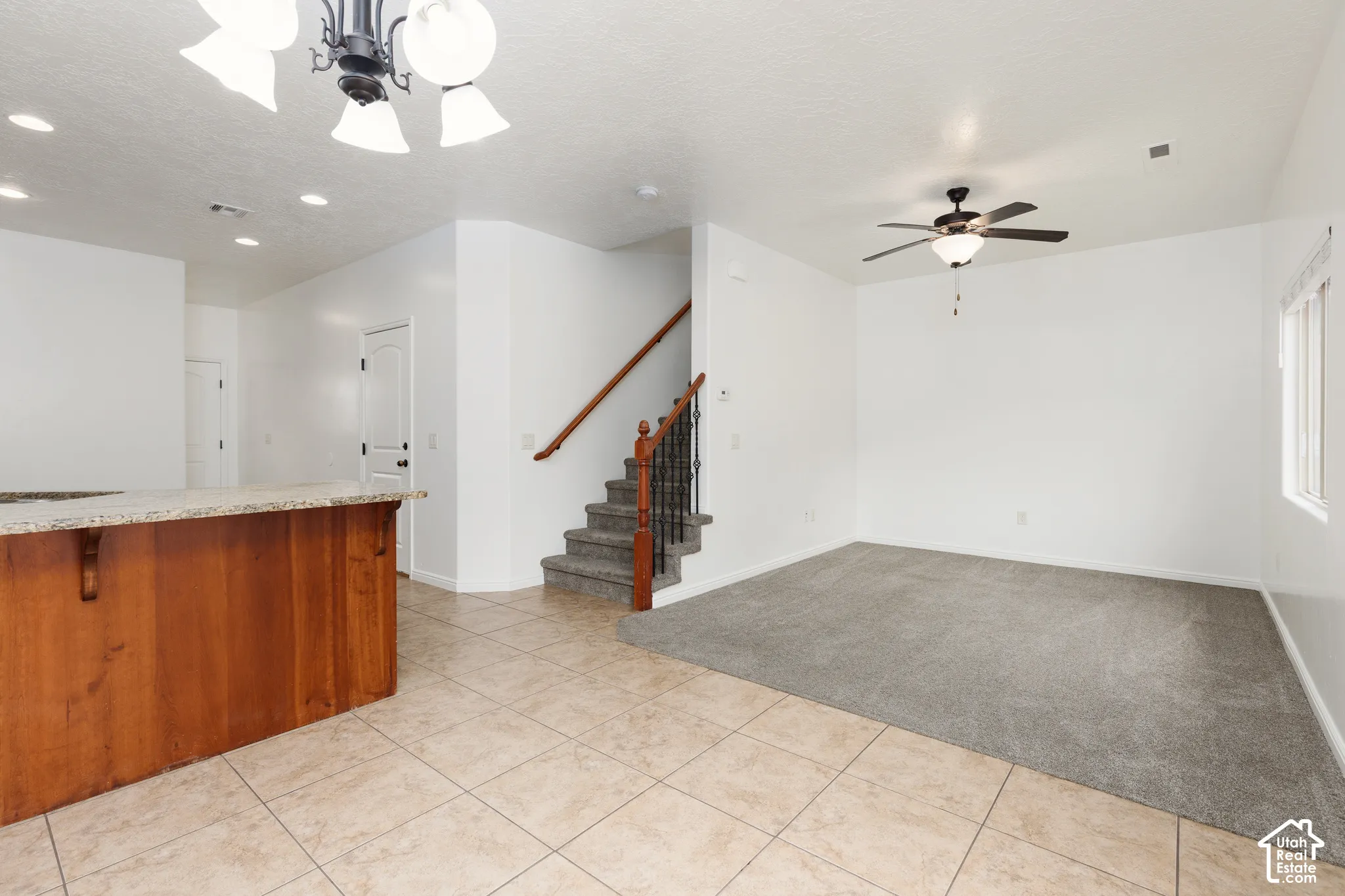 Open-concept living space with tile flooring, a carpeted area, and a staircase featuring wood and wrought iron railing