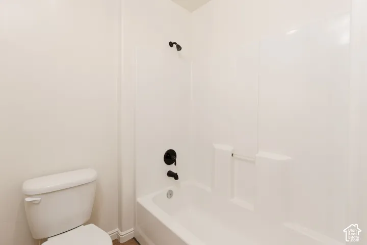 White bathtub with integrated shower, dark bronze fixtures, and a white toilet