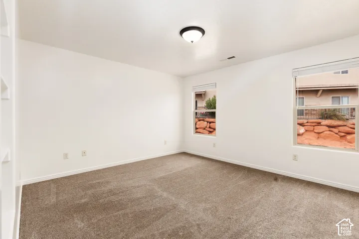 Recessed built-in shelving, neutral-toned carpeting, white walls, and two windows with blinds