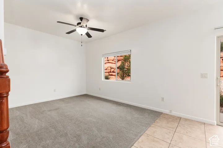Expansive room featuring a ceiling fan with integrated lighting, a window with exterior rock formations, a glass-paned door, carpeting, and tile flooring
