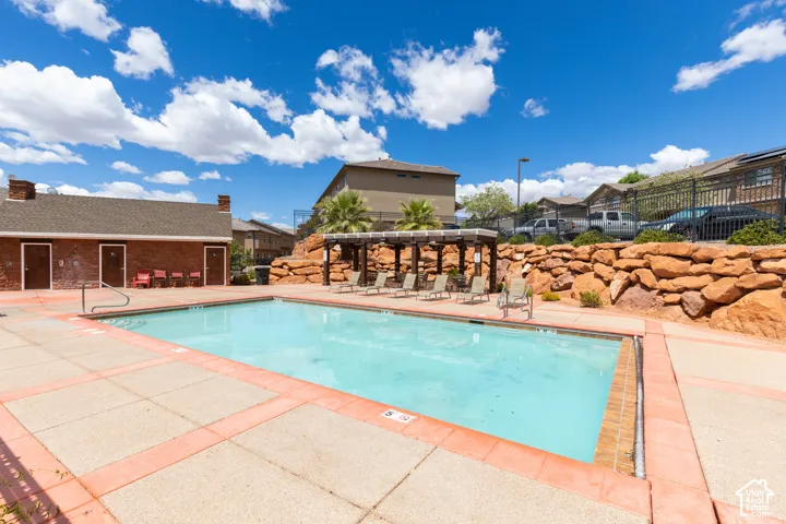 Outdoor swimming pool with concrete decking, a pergola, and a rock retaining wall